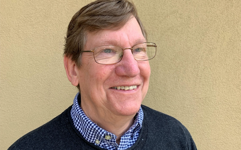 Dave Zilkoski looks off into the distance. He is wearing glasses and a blue checkered button-down shirt with a navy sweater over top.