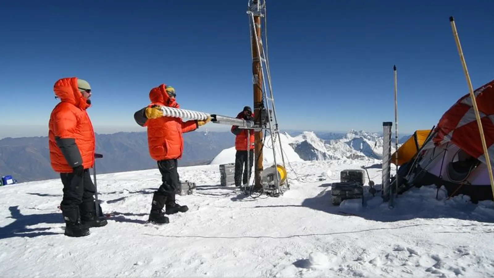 A researcher in an orange coat holds a freshly drilled ice core.