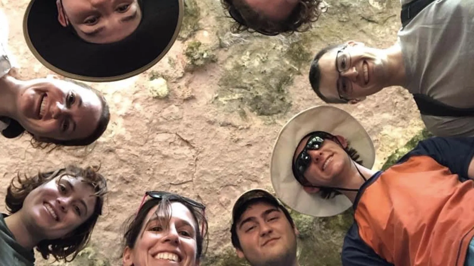 Group photo in a cave, all participants are looking down at the camera with the cave ceiling above everyone
