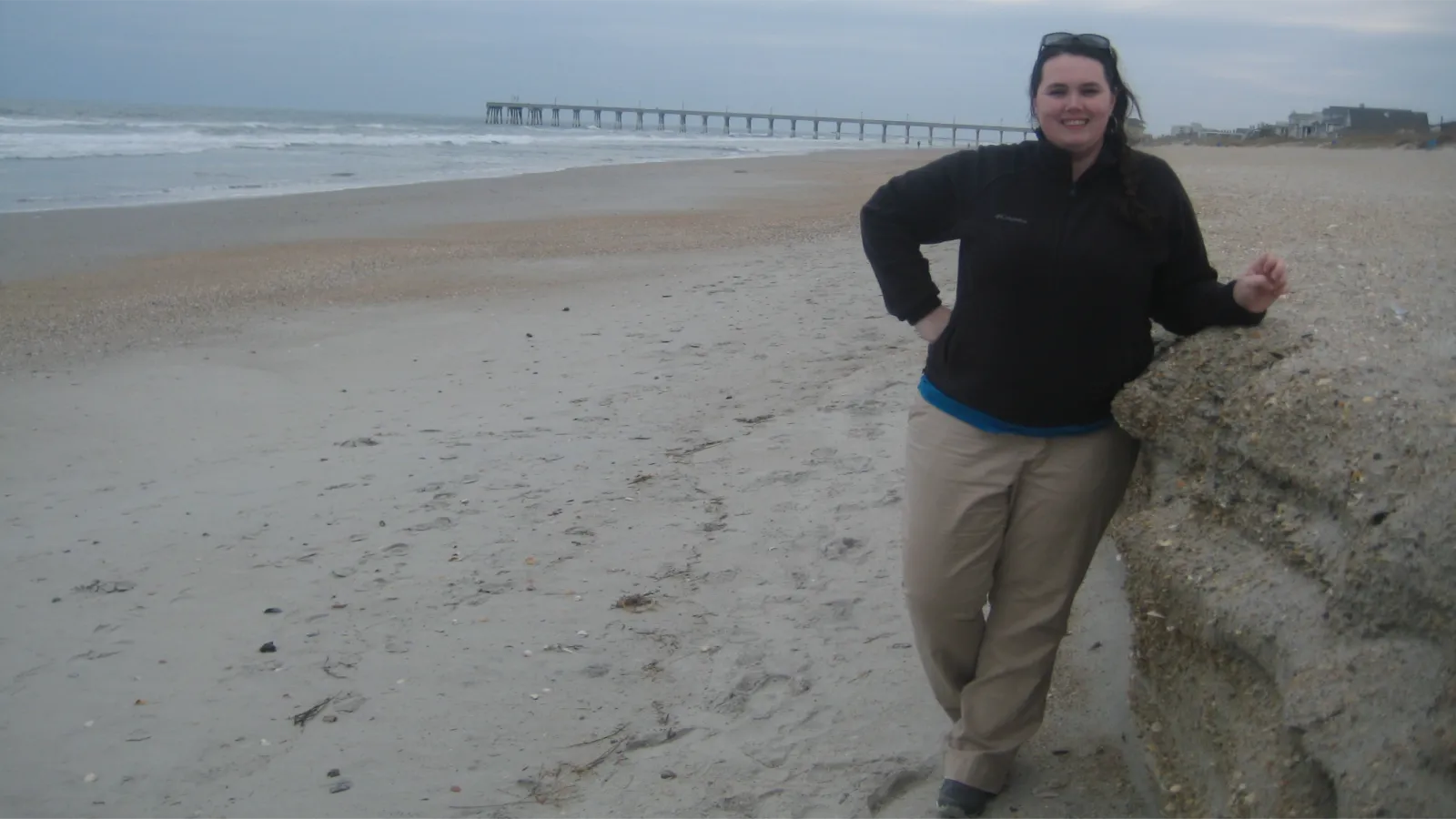 Kelly leans against a rock wall on a beach