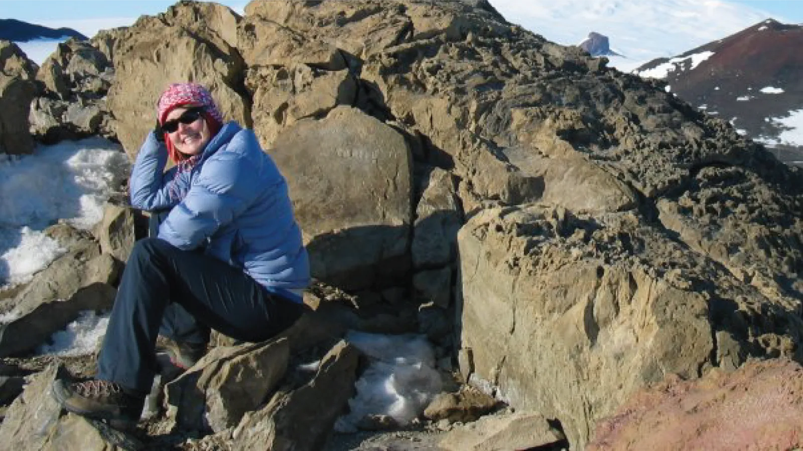 Liz Miller sits on a rock in the mountains and smiles