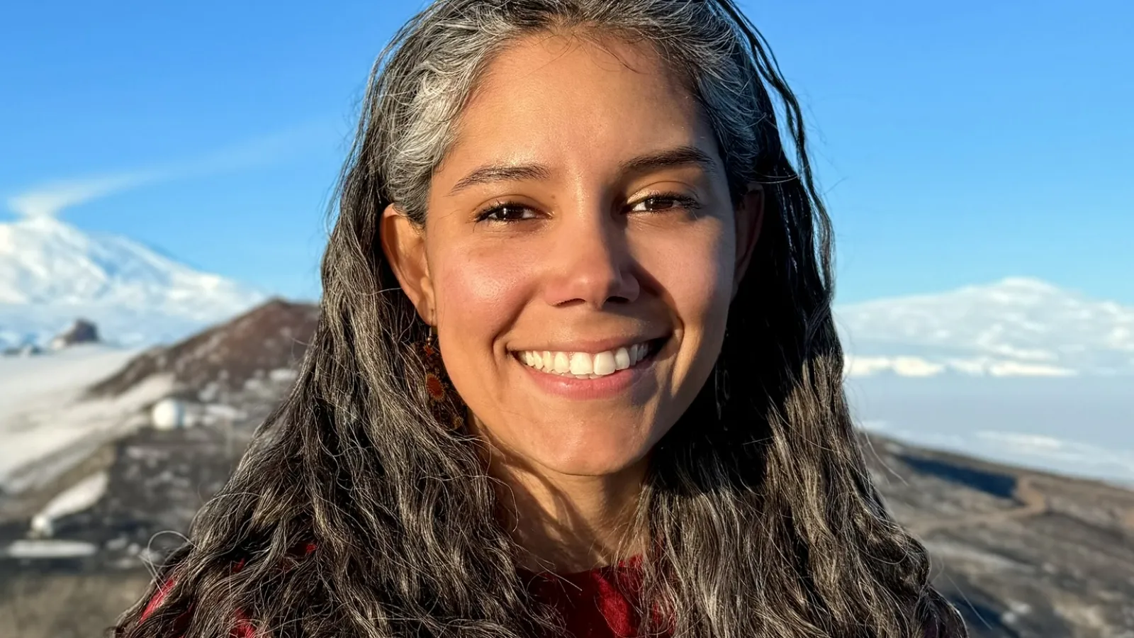 Dr. Melisa Diaz in Antarctica with Mt. Erebus and Mt. Terror in the background