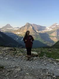Kara Lamantia stands at top of a mountain and other mountains can be seen behind her