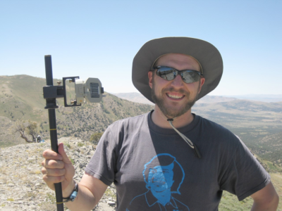 Cole Edwards wearing a hat and sunglasses poses on top of mountain