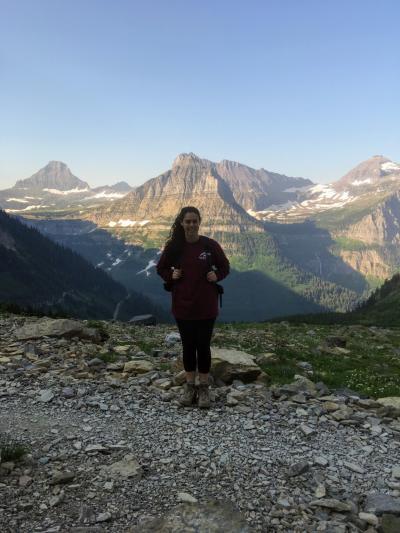 Kara Lamantia stands at top of a mountain and other mountains can be seen behind her