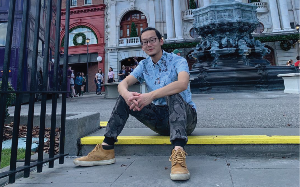 Graduate student Zhaozhe Chen sitting with his hands clasped in front of a statue