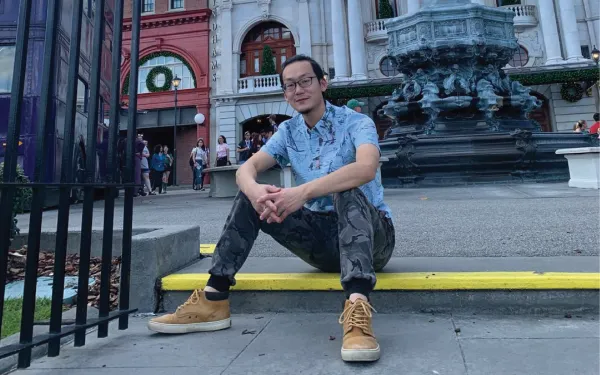 Graduate student Zhaozhe Chen sitting with his hands clasped in front of a statue