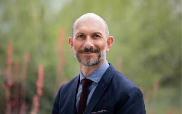 Dr. Louchouarn in a blue suit stands in front of wooded area that is blurred in background