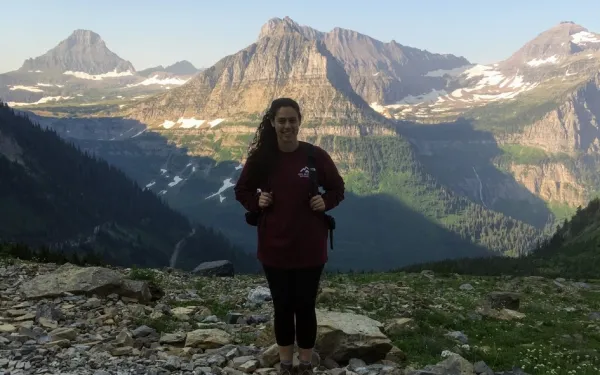 Kara Lamantia stands at top of a mountain and other mountains can be seen behind her