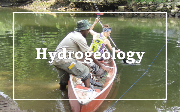 Two students from SES work to collect river water samples from a canoe. Overlain text reads "Hydrogeology".