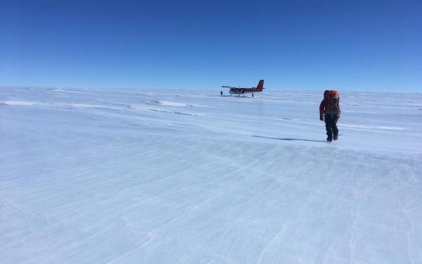  With a pack full of rocks, Mountaineer Scott Barry makes his way toward the Twin Otter aircraft for departure. East Antarctic Ice Sheet and Polar Plateau in the distance, with the nearest outcrop over 1,000 miles away along the Atlantic/Indian sector of Antarctica.