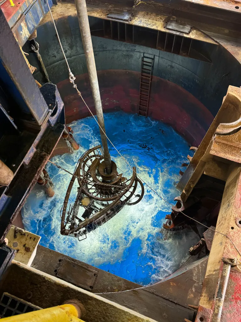 The vibration isolated television (VIT) system in the moonpool. (Credit: Lisa Crowder, IODP JRSO). The VIT is attached to the drillpipe, and is used to image the seafloor before drilling begins.  The VIT also can be used to guide the end of the drillpipe into a reentry cone, in order to re-enter a borehole after the drill bit has been changed.
