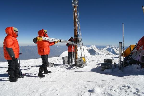 A researcher in an orange coat holds a freshly drilled ice core.