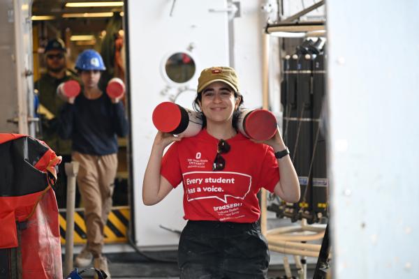 Batoul walking while carrying two sections of a jumbo piston core.