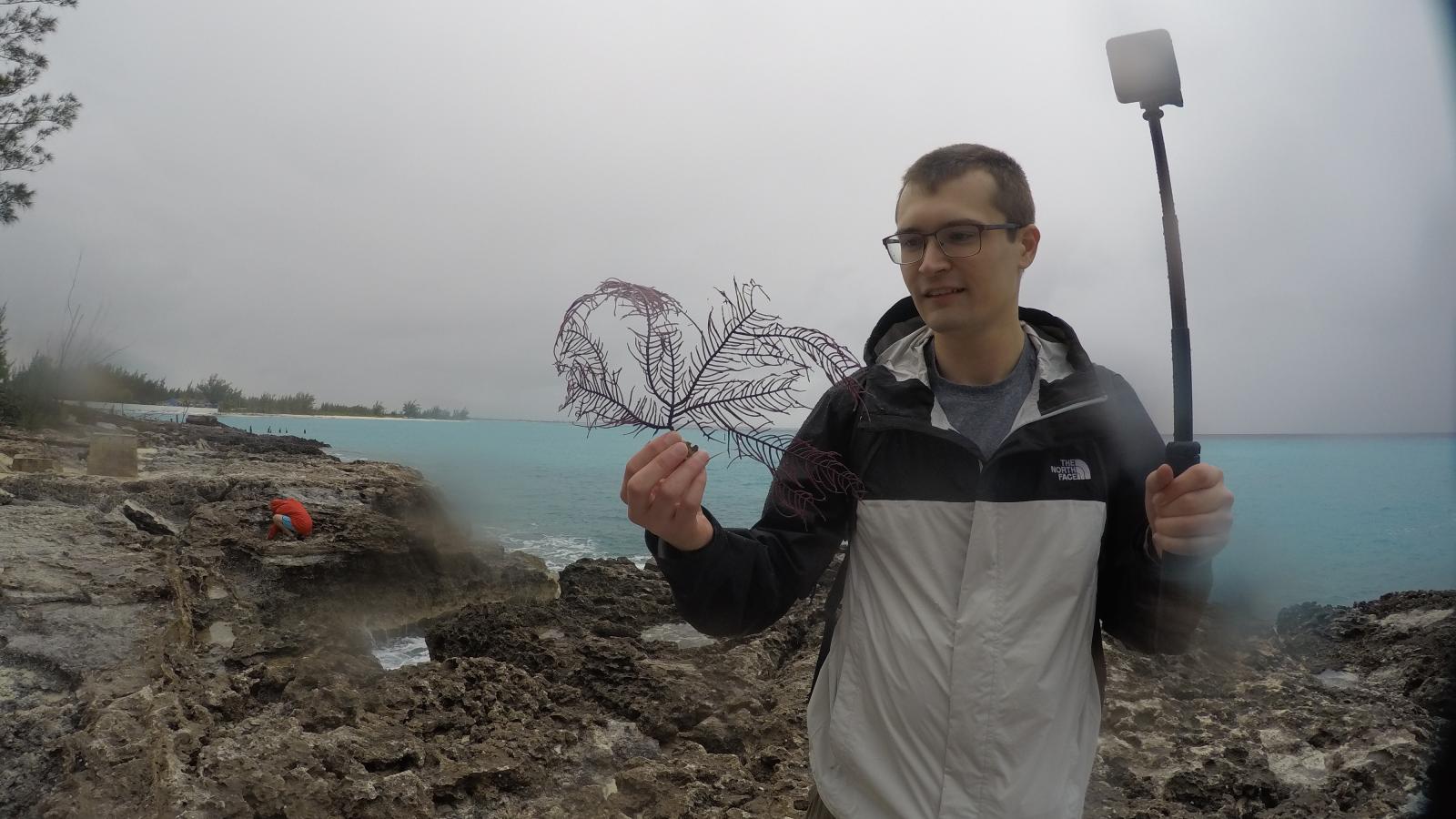 Prescott Vayda examines algae on the beach while holding a gopro on a rainy day