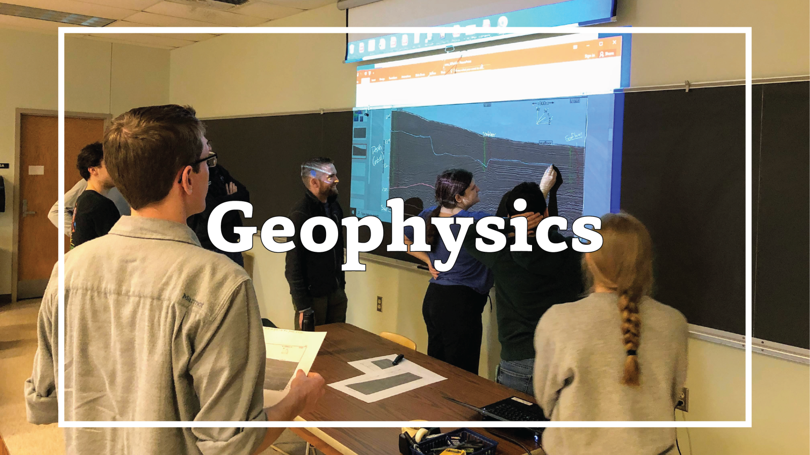 Photo of students in class interpreting seismic data on a projection. Overlain text that reads, "Geophysics"