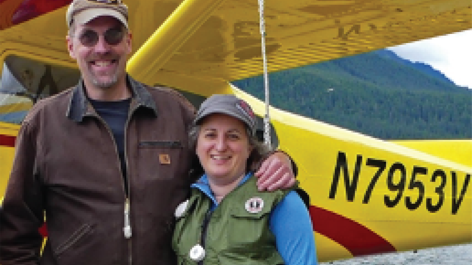 Photo of Jeff DeFreest and his wife in front of a yellow propeller plane in Alaska