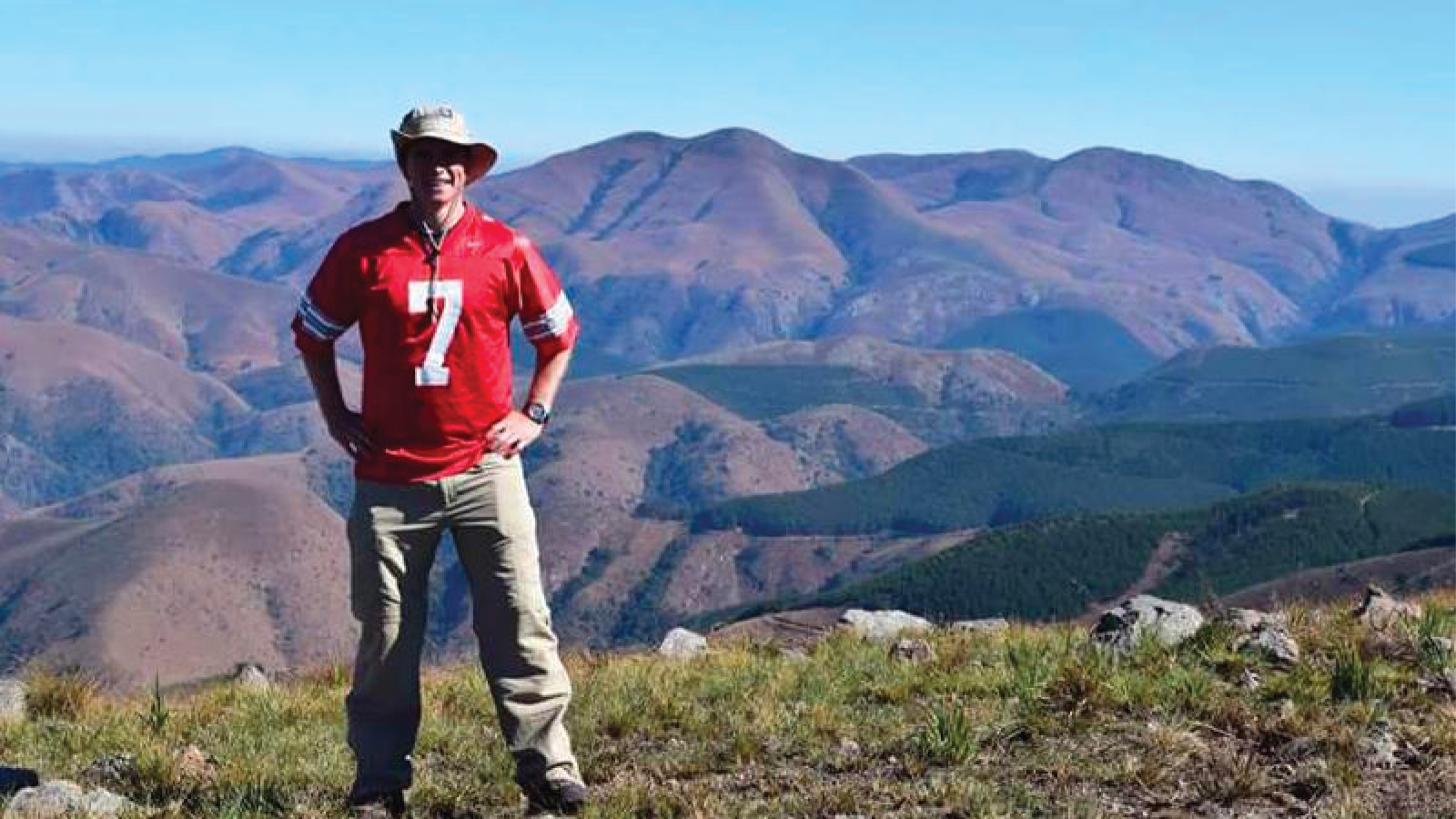 Jake Harrington hiking in the mountains in a hat wearing an OSU jersey