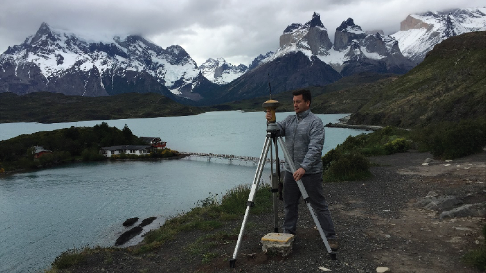 Julio carries out field work in front of a blue mountain lake