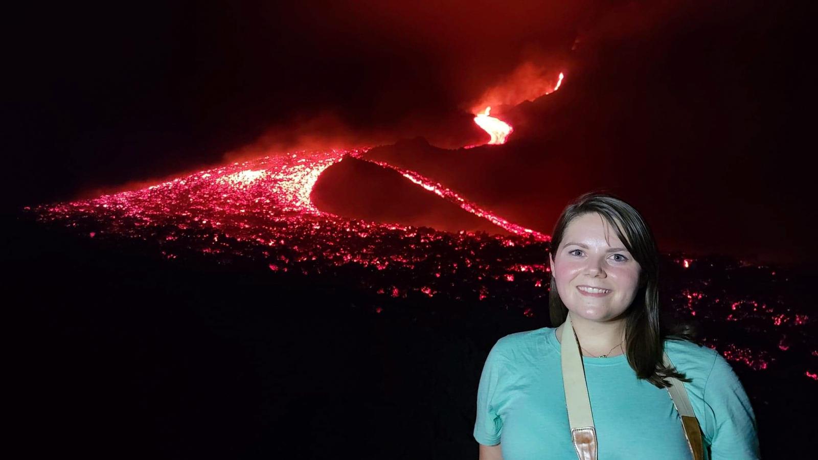 Lindsey on Pacaya Volcano, Guatemala, at night time with an iridescent river of lava