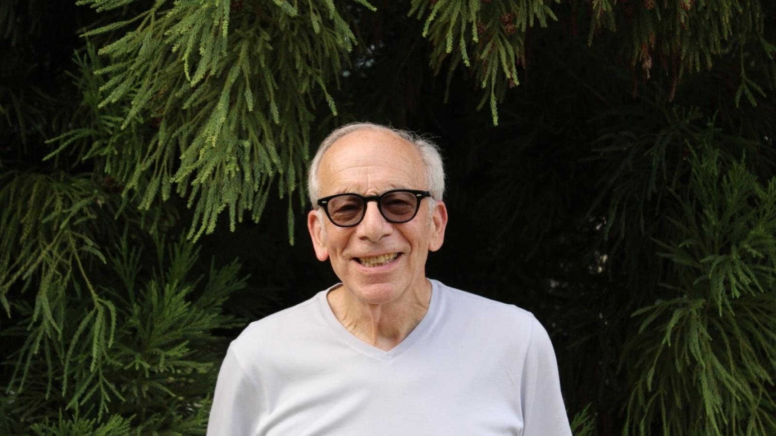 Bruce Hulman in a grey t shirt and darkened glasses in front of trees